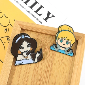 Close-up of Jasmine and Cinderella chibi enamel pins on a light wooden display tray