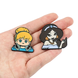 Detailed view of Cinderella and Jasmine enamel pins held by hand for size reference