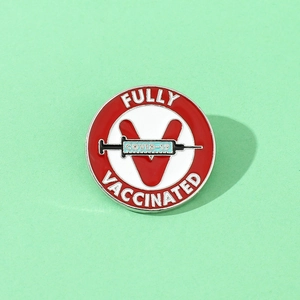 Close-up of circular Fully Vaccinated COVID-19 enamel pin with syringe design on green background