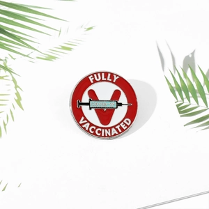 Detailed close-up of a Fully Vaccinated enamel pin with red V logo and COVID-19 syringe design