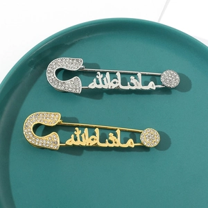 Close-up of gold and silver Mashallah brooches with sparkling rhinestones on green ceramic