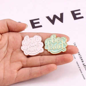 Close-up of enamel pins featuring 'have faith' and 'be kind' in gold artistic lettering