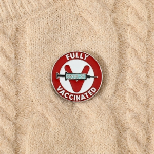 Macro detail of alloy COVID-19 vaccine badge pinned on a beige knitted sweater