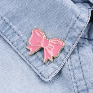 Detail view of a pink enamel bow brooch with gold trim on a blue denim shirt collar
