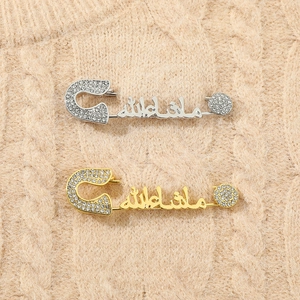 Close-up of gold and silver Mashallah brooches with white rhinestones on knit fabric
