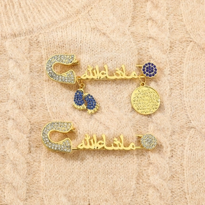 Close-up of golden safety pin brooches with Arabic calligraphy and blue rhinestone charms