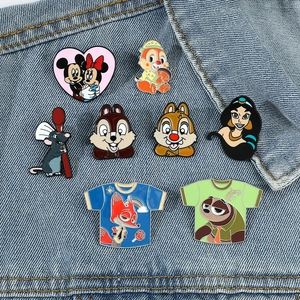 Set of eight cartoon enamel pins displayed on a blue denim jacket pocket detail