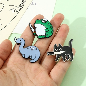 Detailopname van cartoon emaille speldjes met kikker, kat en dinosaurus op een palm