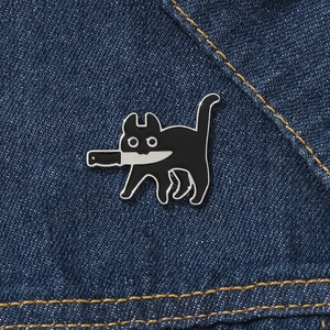 Broche créative en émail chat noir avec couteau sur fond de tissu denim bleu