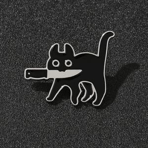 Détail macro du pin's émaillé chat noir avec couteau sur une surface en tissu gris