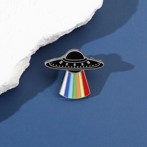 Macro shot of UFO enamel pin with vibrant rainbow light beam detail on a blue background
