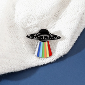 Detailed view of a UFO enamel pin with rainbow beam on a white knit and blue background