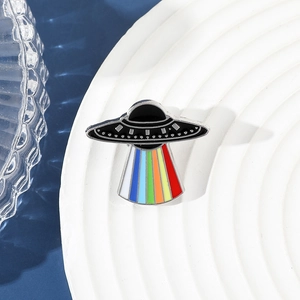 Macro detail of UFO enamel pin with vibrant rainbow light beam on a white tray