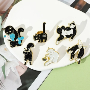Detailed view of six cute cartoon cat enamel pins in black and white on a white ceramic plate
