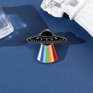 Macro view of a black UFO enamel pin with a colorful rainbow beam on a blue background