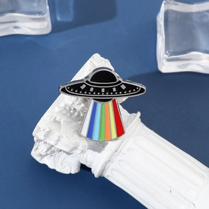 Macro detail of UFO enamel pin with rainbow beam on white decorative stone pedestal