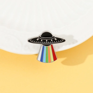 Detail of UFO enamel pin featuring rainbow light beam on a bright yellow background