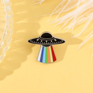 Detail of UFO enamel pin featuring black flying saucer with vibrant rainbow light beam