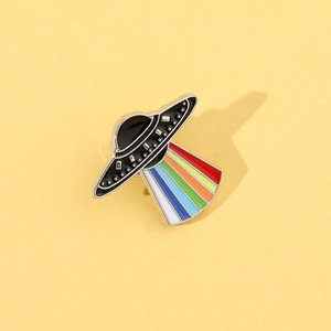 Close-up of UFO enamel pin with vibrant rainbow beam detail on a yellow background