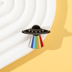 Close-up of a cartoon UFO enamel pin with vibrant rainbow beam on a wavy base