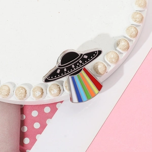 Macro view of cartoon UFO enamel pin with vibrant rainbow beam and black metal finish