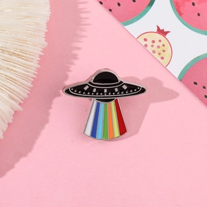 Close-up of a UFO enamel pin featuring a vibrant rainbow light beam on pink surface