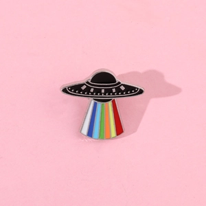 Detail of UFO enamel pin with vibrant rainbow beam on a soft pink textured background