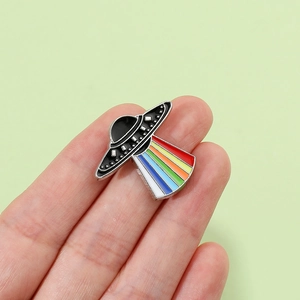 Macro view of UFO enamel pin with vibrant rainbow light beam and metallic edges