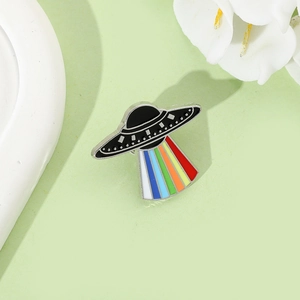 Detailed view of UFO enamel pin with vibrant rainbow light beam on green background