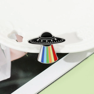 Macro view of UFO enamel pin with vibrant rainbow beam on white ceramic decorative plate