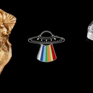 Detailed view of a black UFO enamel pin featuring a vibrant rainbow light beam design