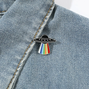 Cartoon UFO enamel pin with rainbow beam on blue denim jacket, space cosmic theme metal badge