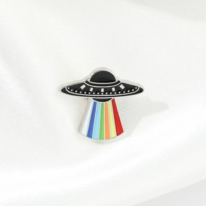 Detail of UFO enamel pin with colorful rainbow light beam on white silk background