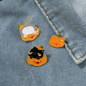 Three Halloween enamel pins featuring cute cats and pumpkins on blue denim fabric background