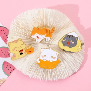 Dettaglio di quattro spillette in smalto a forma di gatto su vassoio e sfondo rosa