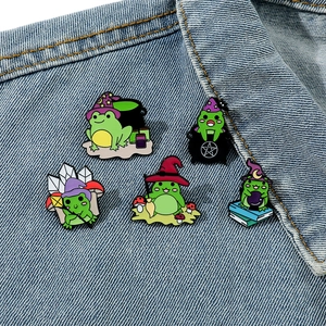 Five-piece set of cartoon wizard frog enamel pins on blue denim fabric background
