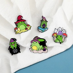 Detailed set of five cartoon magic frog enamel pins with wizard hats on white fabric