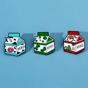 Vue détaillée de trois épingles en émail de briques de lait avec motifs vache, grenouille et Noël