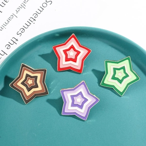 Macro view of four colorful star-shaped enamel pins with layered metal frames in a dish