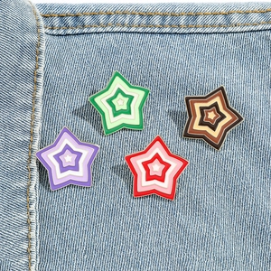 Set of four colorful gradient star enamel brooches on blue denim fabric background