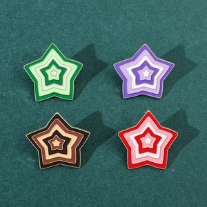 Detailed view of four colorful gradient star enamel pins on a dark green textured fabric