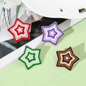 Close-up of four gradient star enamel pins on a white ceramic plate and green card