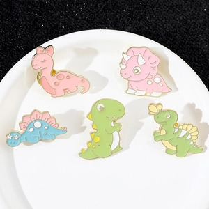 Set di cinque spille smaltate a forma di dinosauro colorato su un vassoio bianco tondo