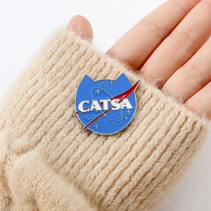 Detail of blue enamel CATSA cat pin held against a beige knitted sweater background