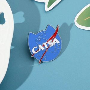 Close-up of a blue NASA-style enamel cat pin with CATSA text and metallic finish