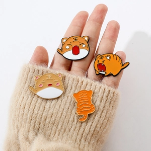 Detailed view of four cartoon tiger enamel pins held against a beige knitted sweater
