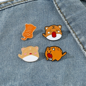 Detailed view of four cute tiger enamel pins neatly arranged on blue denim fabric background