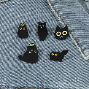 Cute black cat enamel pins set featuring 5 diverse kitten expressions on denim jacket
