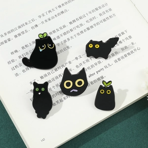 Set of five cartoon black cat enamel pins displayed on an open book for decoration