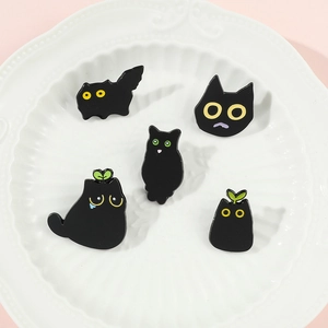 Close-up of a five-piece set of cute black cat enamel pins displayed on a white ceramic plate